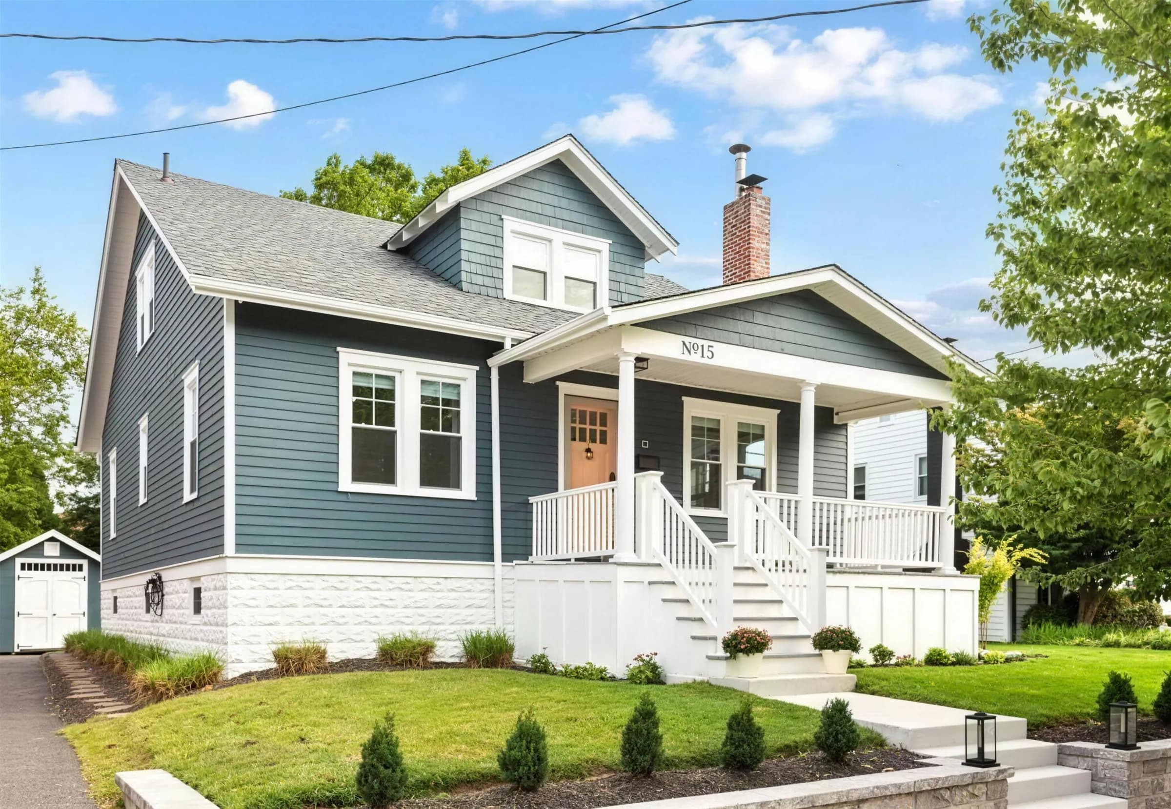 A blue craftsman house with a white front porch and a landscaped lawn