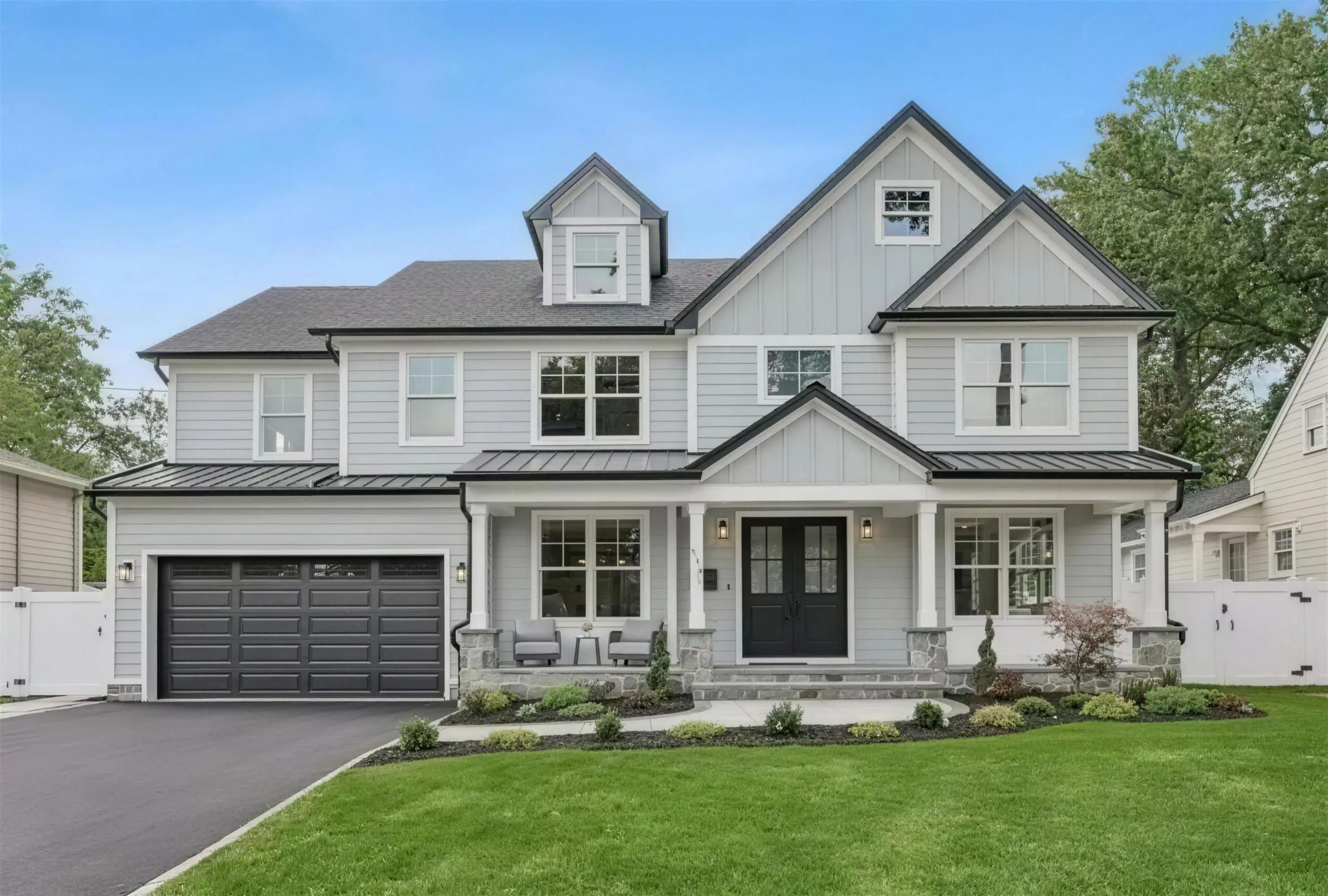A modern farmhouse-style home with a covered porch, a two-car garage and a green lawn