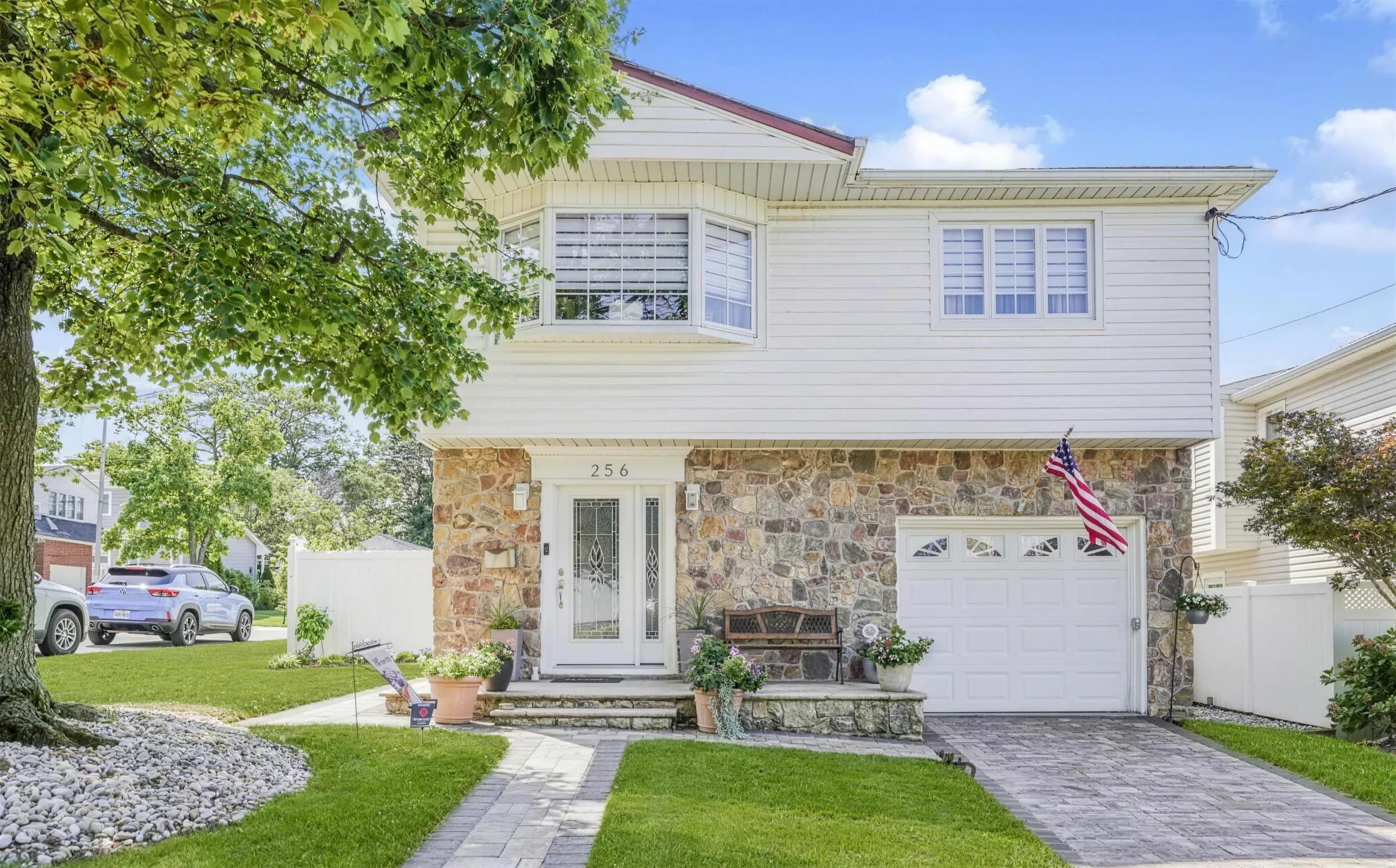 A two-story house with a stone front, a single garage and a paver walk across the lawn