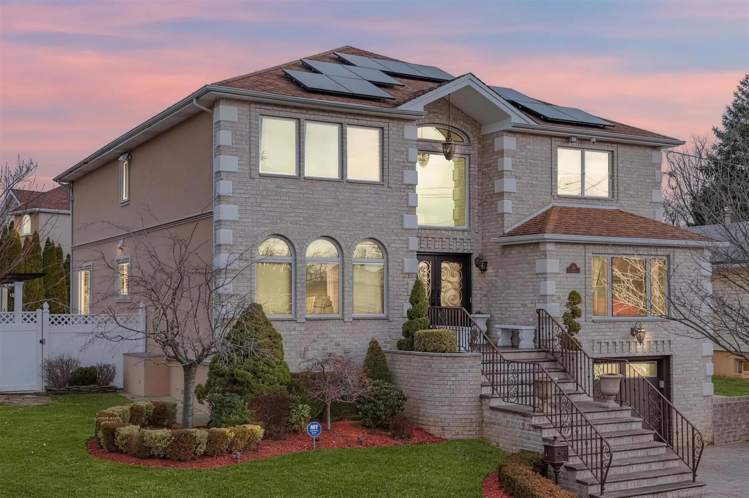 A brick and stone two-story house with arched windows and a curved stoop at dusk