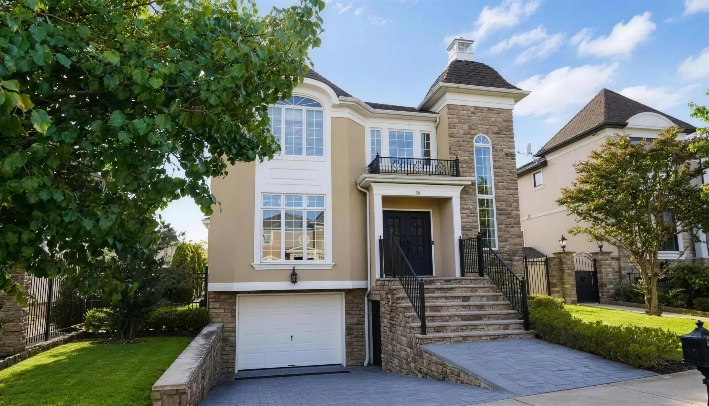 A stone and stucco house with a front balcony, a wide stoop and a paver driveway